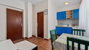 A compact kitchen with blue cabinets, a tiled backsplash, and a small dining area with a table and chairs. - Apartment Šibenik near Beach Gaj (Šibenik-Brodarica)
