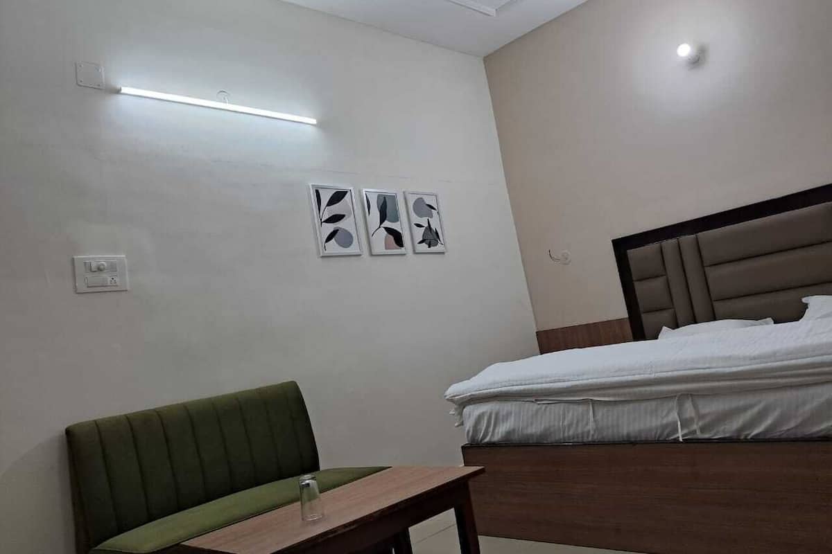 Quarto de hotel com cama, sofá verde, mesa pequena e três obras de arte na parede.