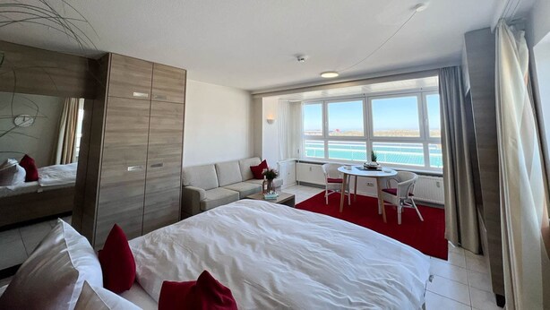 Une chambre d’hôtel avec un grand lit, un canapé, une table à manger et une vue sur la mer.