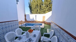 Un patio con piscina, sillas blancas y una mesa lista para una comida.