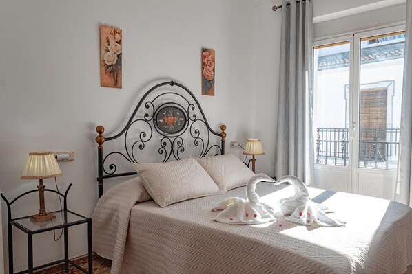 Una cama bien hecha con un cisne decorativo, dos lámparas de pared y dos cuadros florales.