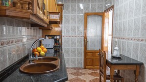 Una cocina con encimera de granito, un fregadero, un mueble de madera, una mesita con una silla y una puerta que da a otra habitación.