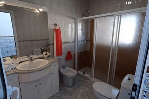 A bathroom with a sink, bidet, toilet, and a shower area.