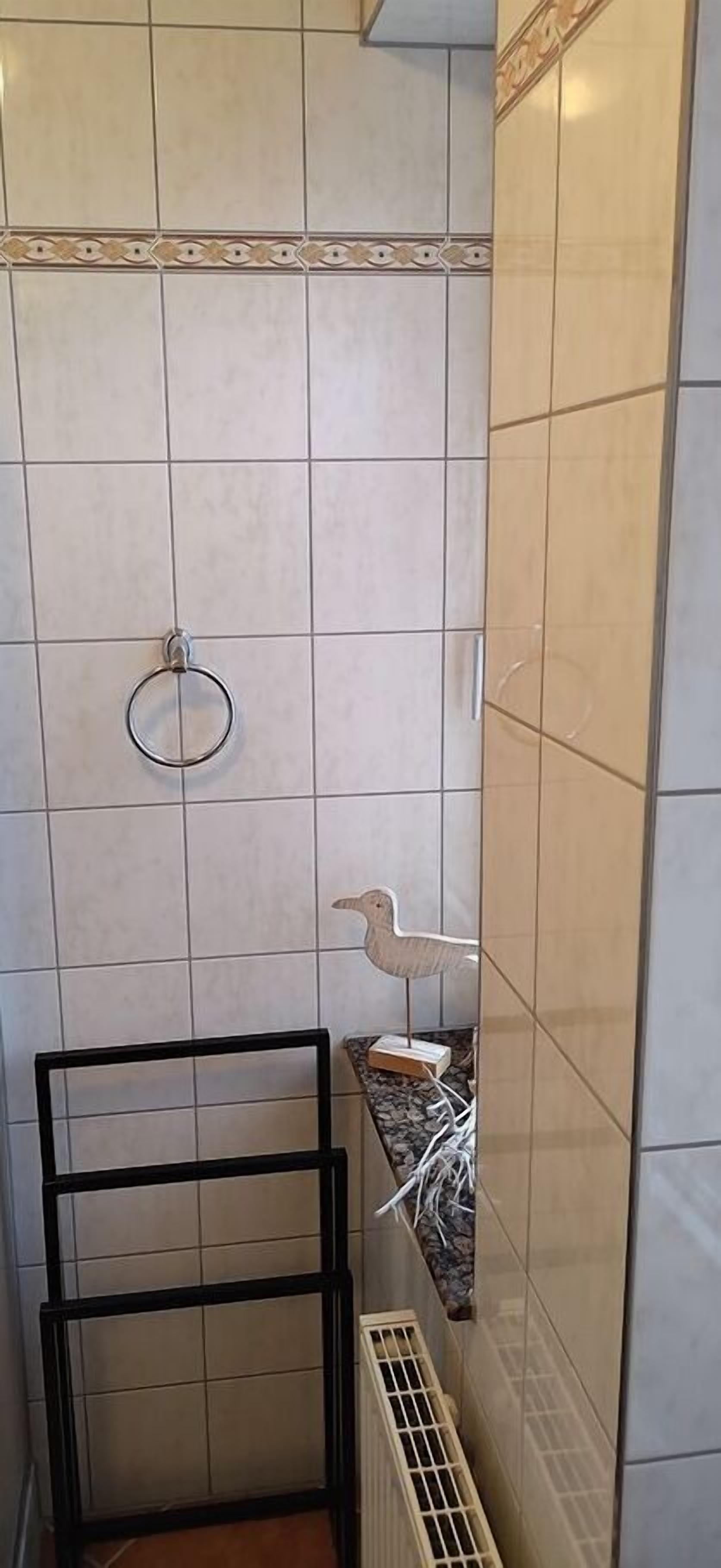A bathroom with white tiles, a towel ring, a small shelf with a decorative item, and a black metal rack.