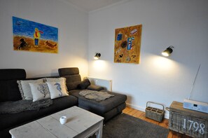 Una sala de estar con un sofá gris, una mesa de centro blanca y dos lámparas fijadas a la pared.