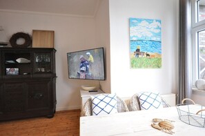 Ein Zimmer mit Fernseher, einem Gemälde, einem Holzkasten und einem Bett mit gemusterten Kissen.