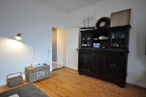 Una habitación con un mueble de madera oscura, cestas de mimbre, una puerta blanca y una lámpara.