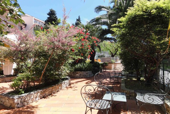 An outdoor patio with stone planters, metal chairs, and a pathway leading to a building.