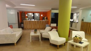 A hotel lobby with a reception desk, seating area, and a small table with a basket of fruit. - Apartment for 5 guests in Pietra Ligure (Pietra Ligure)