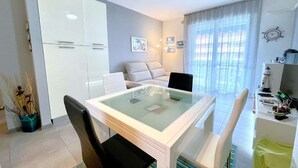 A modern living room with a glass-top dining table, a sofa, and a TV. - Apartment in Porto Santa Margherita near Beach (Porto Santa Margherita (VE))