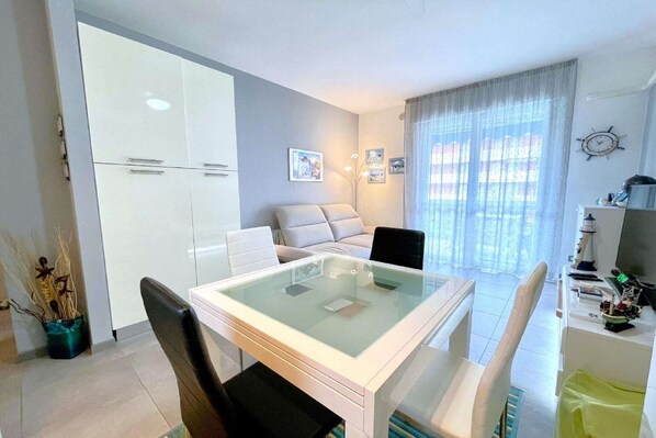 A modern living room with a glass-top dining table, a sofa, and a TV.