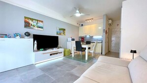 A modern living room with a flat-screen TV, a dining area, and a kitchen. - Apartment in Porto Santa Margherita near Beach (Porto Santa Margherita (VE))