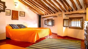 A room with a bed, wooden beams on the ceiling, a window, and a door.
