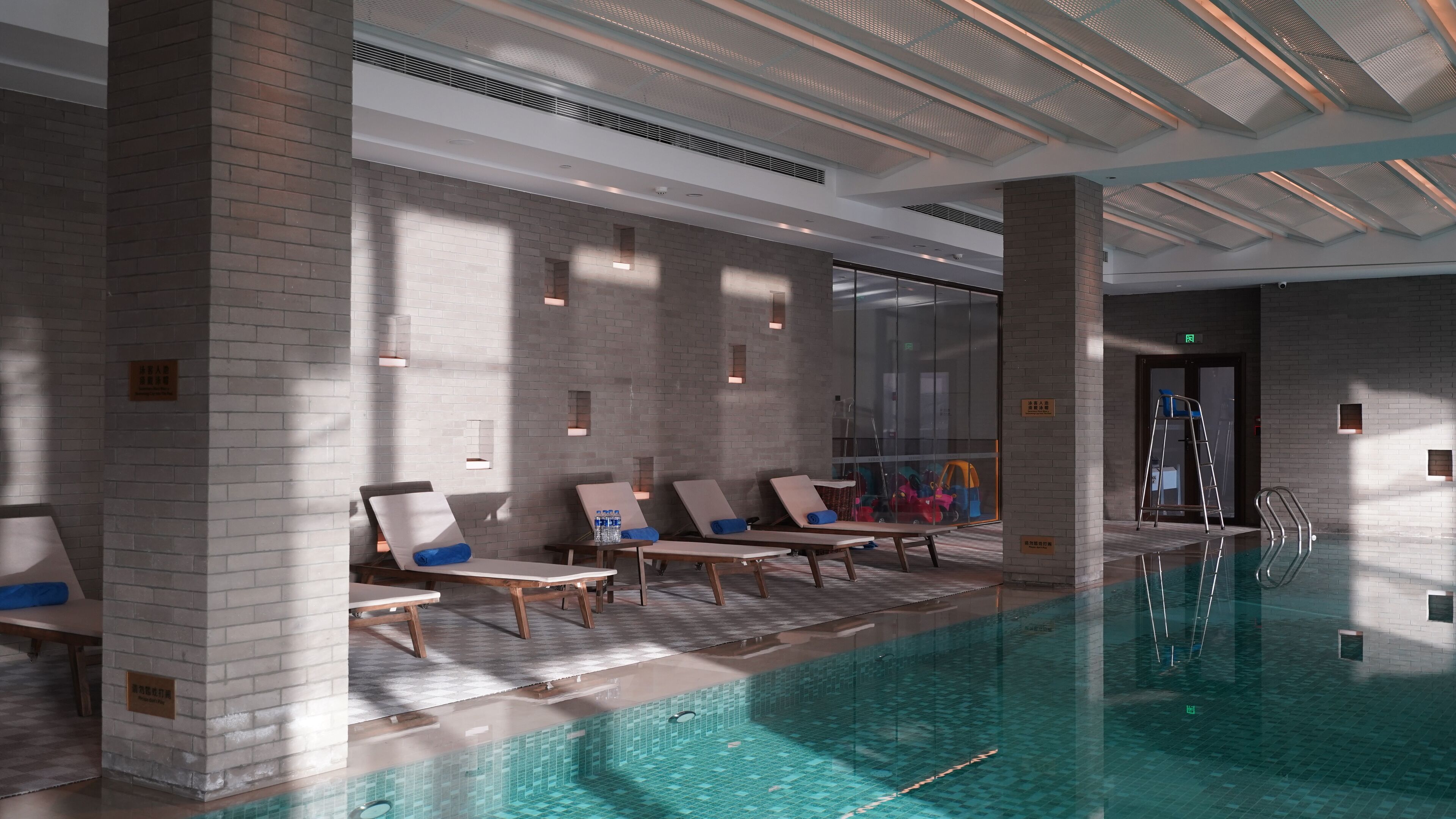 Una piscina interior moderna con sillones de descanso y un muro de cristal.