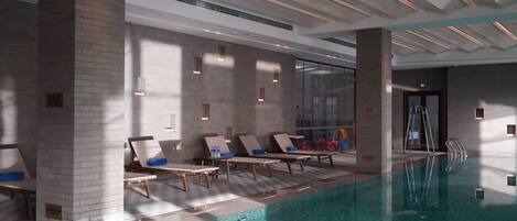 Una piscina interior moderna con sillones de descanso y un muro de cristal.