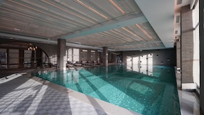 A large indoor swimming pool with a tiled floor and ceiling, surrounded by lounge areas with chairs and sun loungers. - WANDA REALM Yan'an (Yan'an)