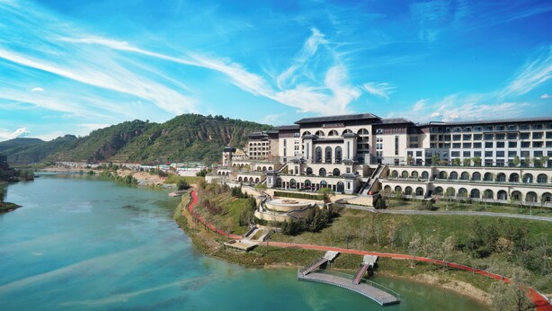 A large hotel with multiple buildings, a river in the foreground, and a bridge connecting the buildings. - WANDA REALM Yan'an (Yan'an)