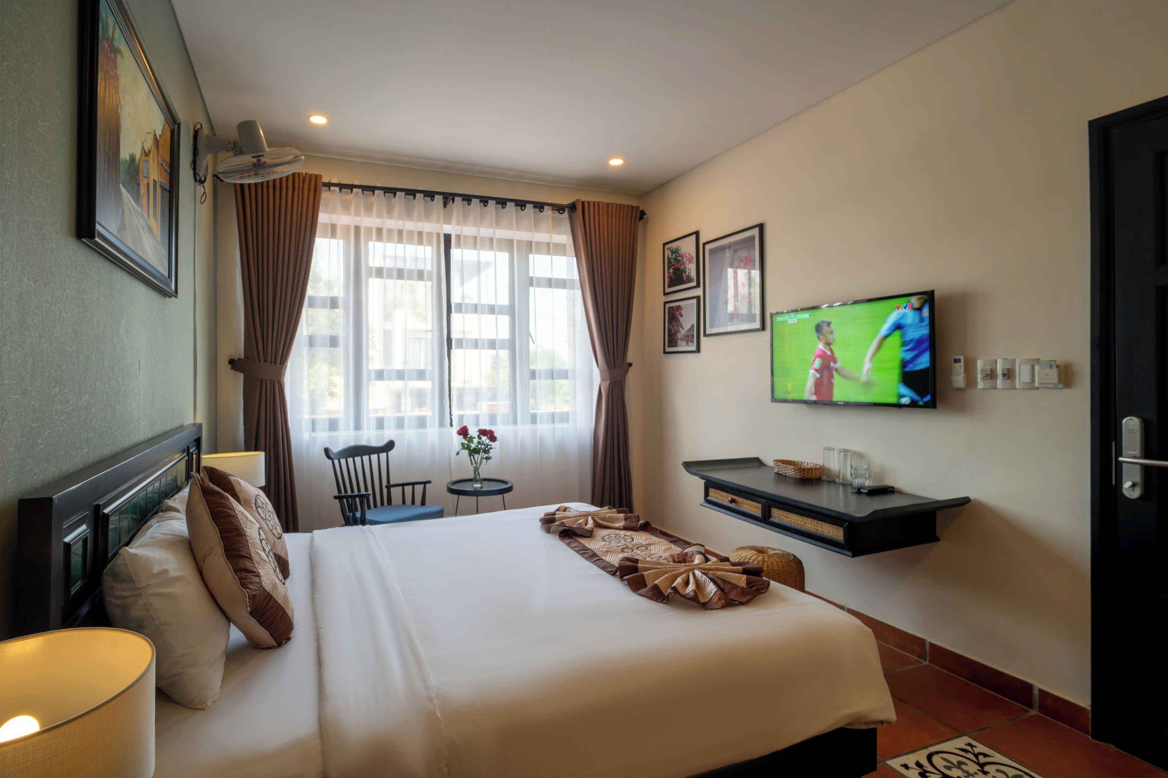 Habitación de hotel con una cama grande, un televisor en la pared, un escritorio con una silla y una ventana con cortinas.