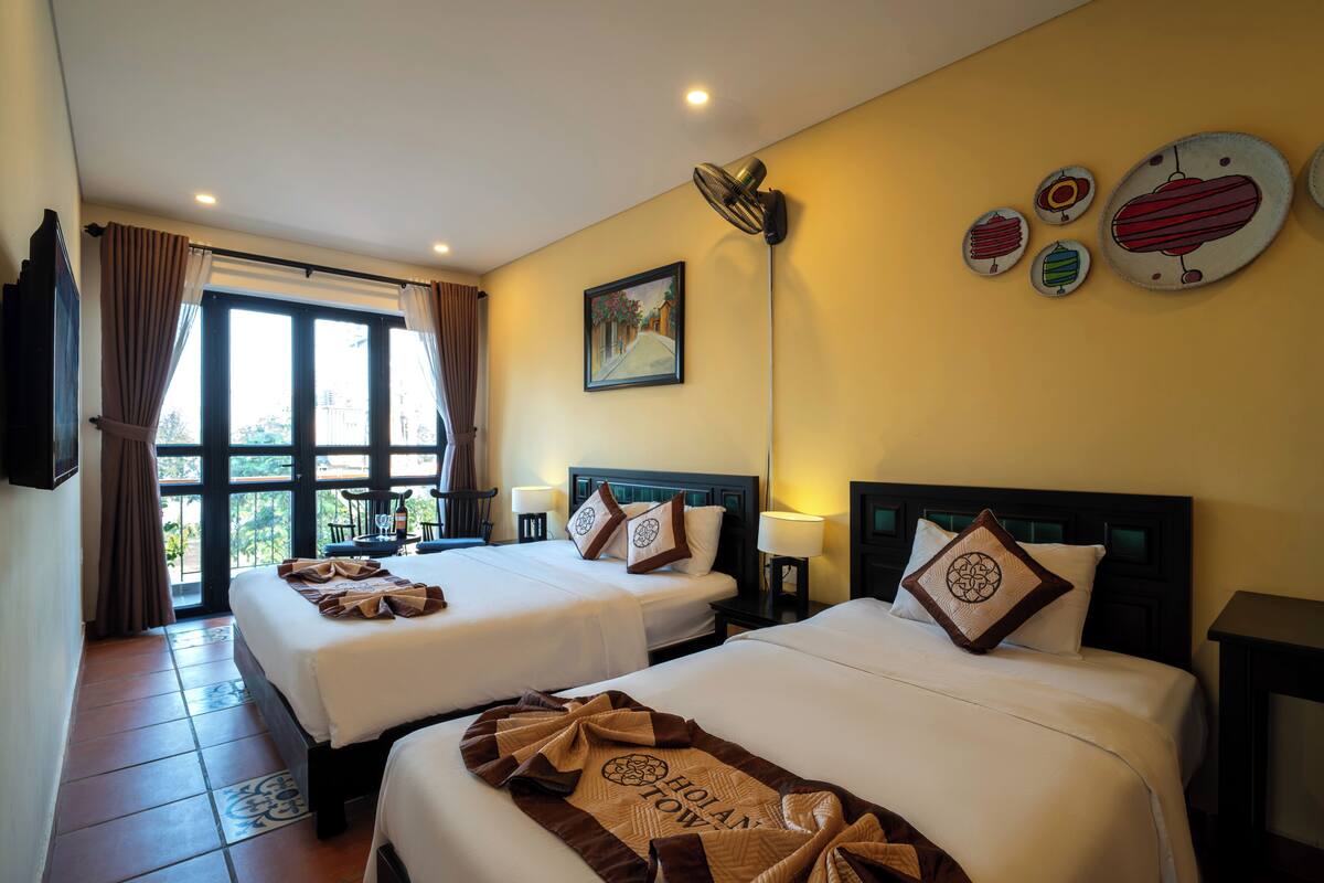 A hotel room with two beds, a large window, a painting on the wall, and a ceiling fan.