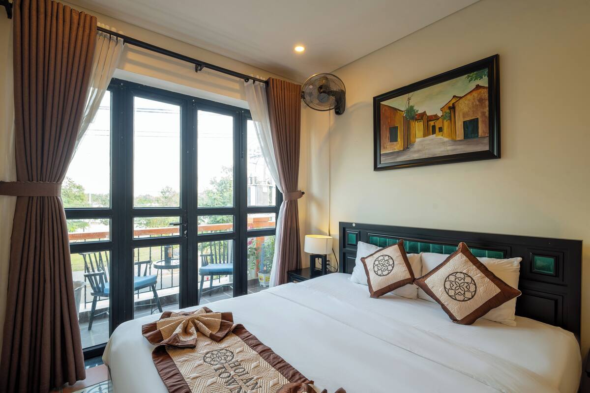 A hotel room with a large bed, a balcony with chairs, and a painting on the wall.