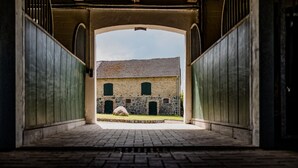 An arched passageway leading to a building with a stone facade and green shutters.
