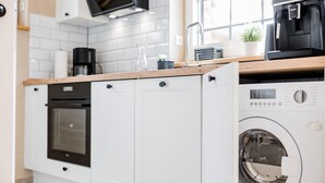 A compact kitchen with a built-in oven, a coffee maker, and a washing machine.