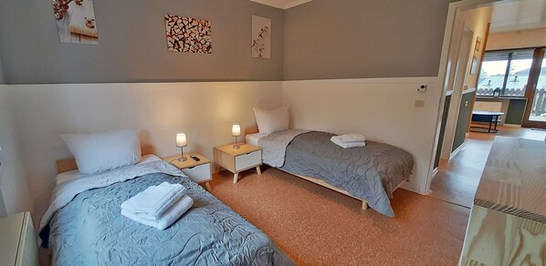 Ett hotellrum med två sängar, var och en med en kudde och en hopvikt handduk. Det finns sängbord med lampor och ett litet bord med en stol i hörnet.