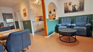Ein Wohnzimmer mit einer Couch, Sesseln, einem Couchtisch und einer Küche im Hintergrund.