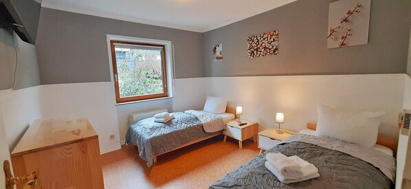 A bedroom with two beds, a window, bedside tables with lamps, and wall art.