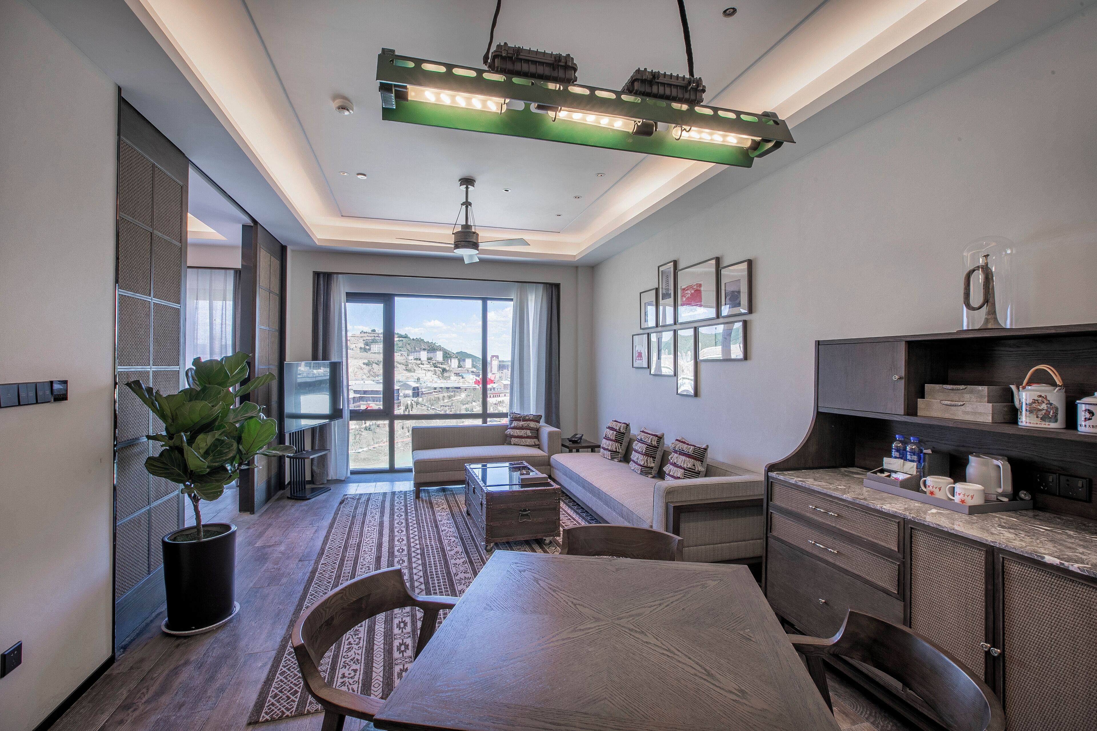 A modern living room with a sofa, dining table, and chairs, a kitchen area with cabinets and a countertop, and large windows offering a view of the city.