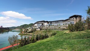 A large hotel with multiple stories, a river in the background, and a green hillside. - WANDA JIN Yan'an (Yan'an)