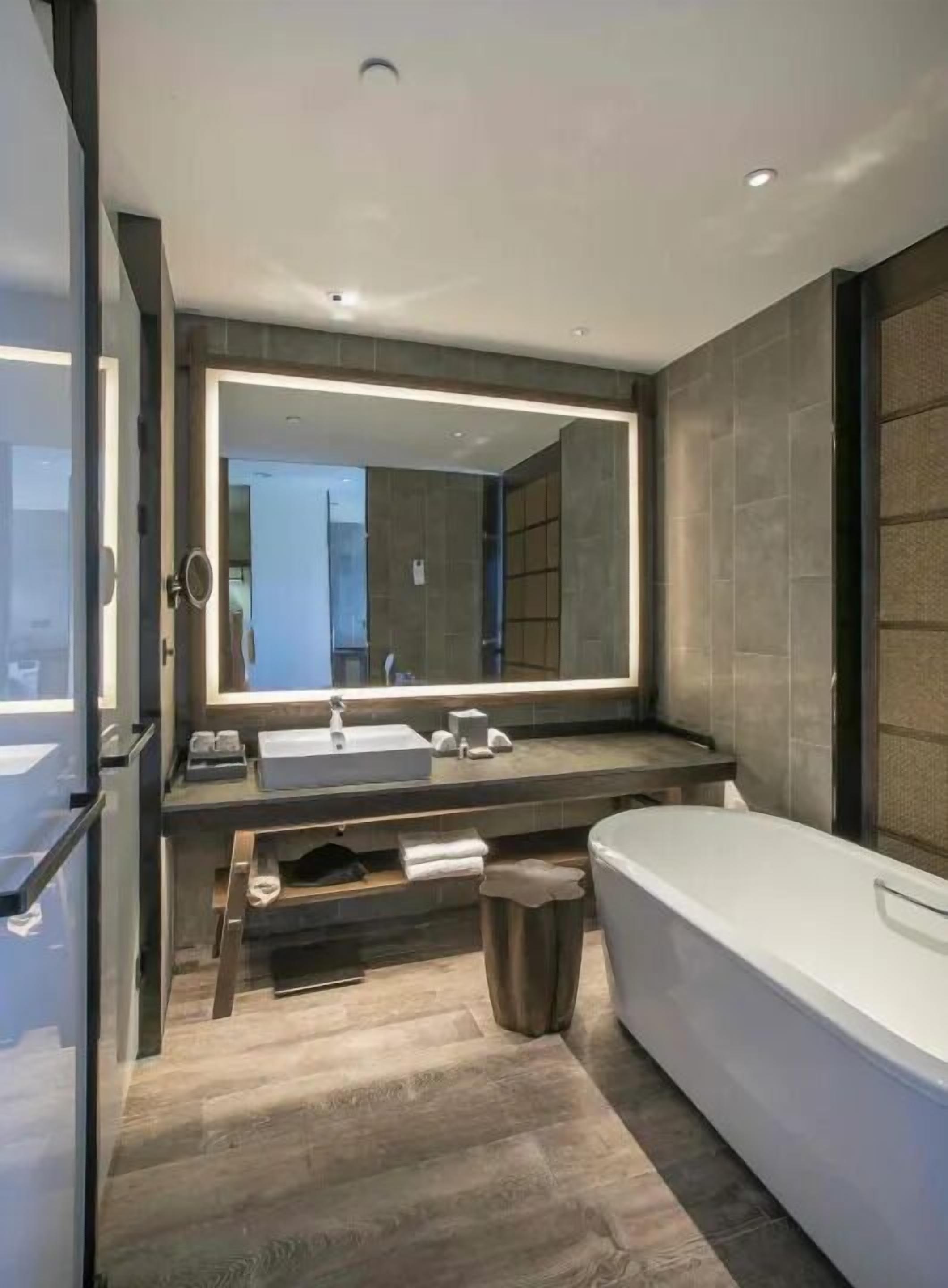 Ein modernes Badezimmer mit großem Spiegel, doppelter Waschbecken, Badewanne und Holzboden.