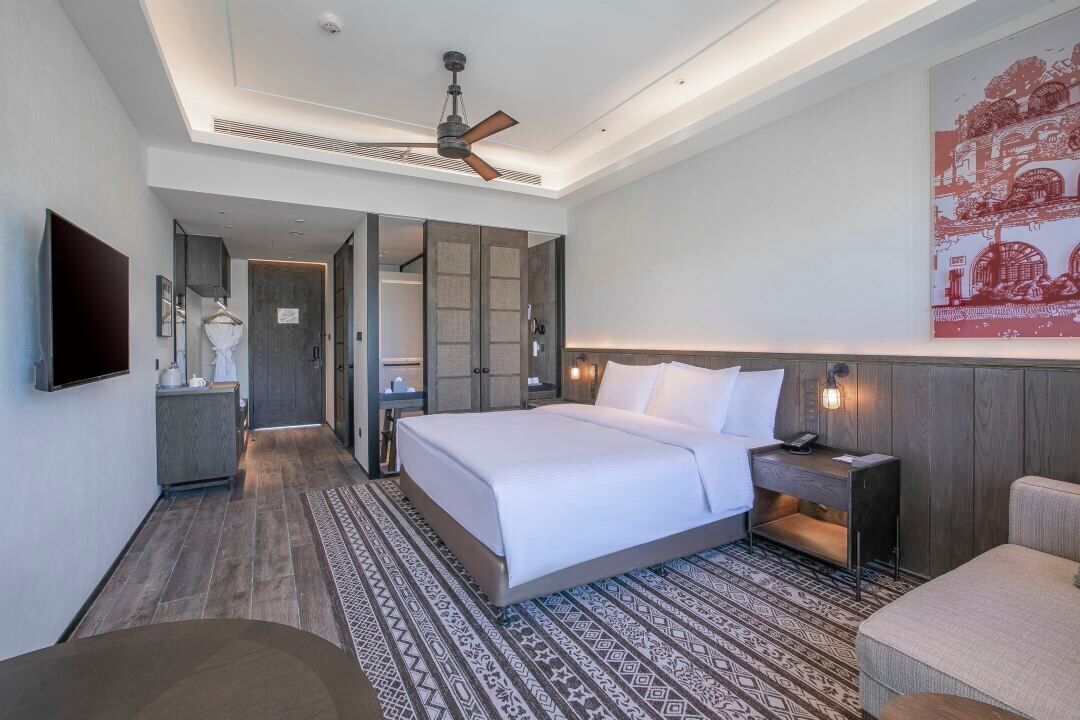 A modern hotel room with a large bed, a flat-screen TV, a bedside table, and a ceiling fan.