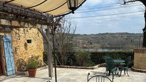 Una mesa con cubierta de vidrio, sillas de metal, un farol colgante y una vista de un lago y colinas al fondo.