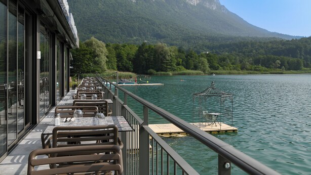 A lakeside restaurant with outdoor seating, overlooking a calm lake and forested mountains. - La Villa du Lac (Aiguebelette-le-Lac)