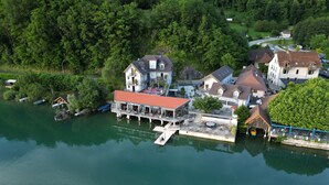 A riverside hotel with a dock, surrounded by lush greenery and multiple buildings. - La Villa du Lac (Aiguebelette-le-Lac)