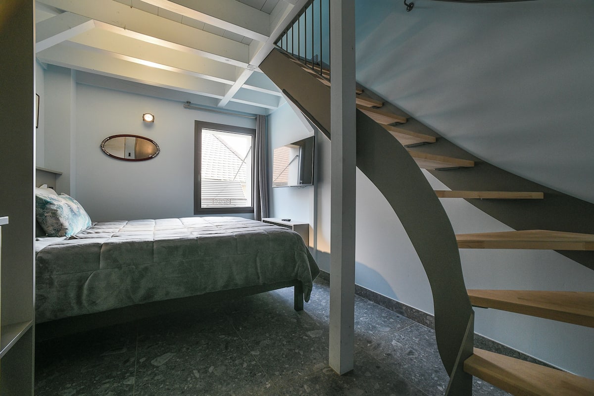 Une chambre à coucher avec un lit, une fenêtre, un miroir et un escalier en bois.