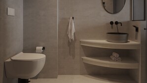 A modern bathroom with a freestanding toilet, a round mirror, and a sink with a basin. - néreya luxury rooms (Rhodes)