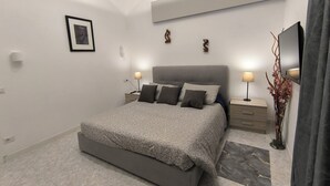 A modern bedroom with a large bed, bedside tables, a flat-screen TV, and a decorative plant.