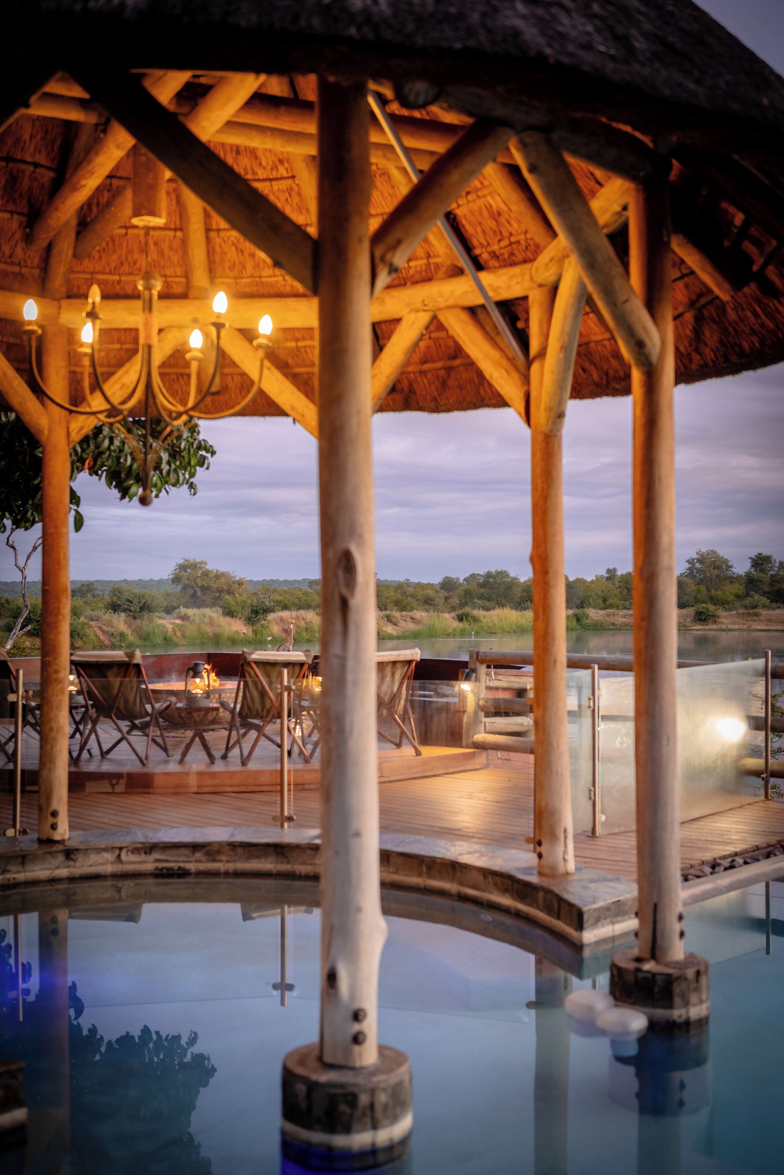An outdoor pool area with wooden deck, lounge chairs, and a thatched roof structure.