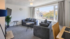 A modern living room with a sofa, a small table, a TV, and a large window with curtains. - Host Stay Park View (Thetford)