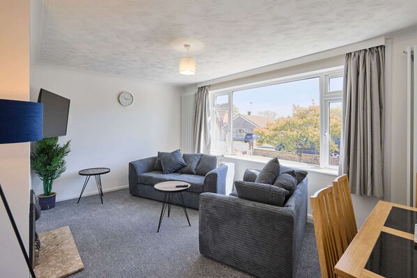 A modern living room with a sofa, a small table, a TV, and a large window with curtains. - Host Stay Park View (Thetford)