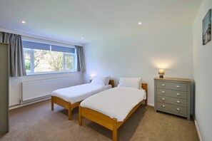 A bedroom with two single beds, a dresser, a radiator, and a window with curtains. - Host Stay Park View (Thetford)