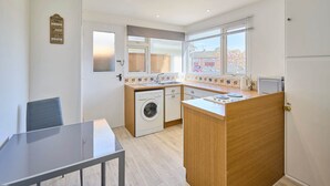 A compact kitchen with a washing machine, a small dining table, and a window with a view of the outside. - Host Stay Park View (Thetford)
