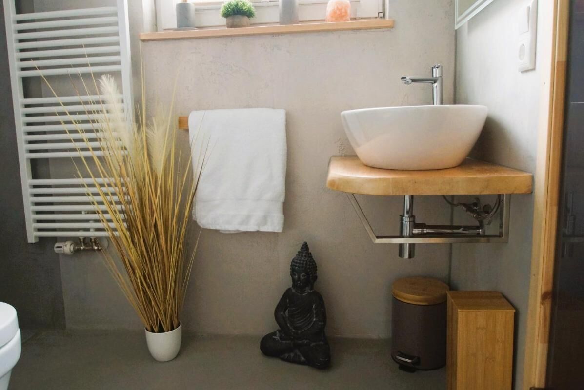 A bathroom with a white sink, a small Buddha statue, and a potted plant.