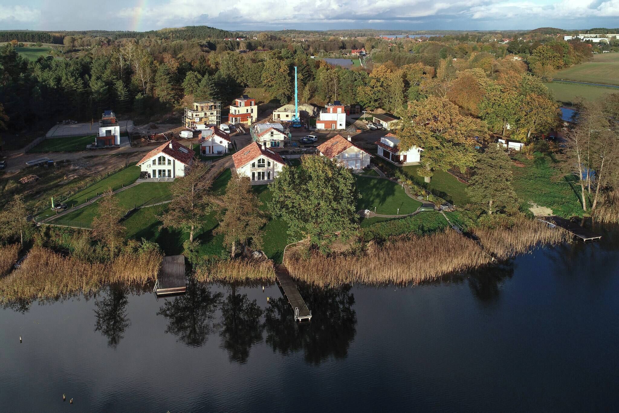 Vue aérienne d’un village au bord d’un lac, avec des maisons, un quai et une haute structure.