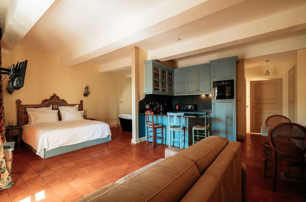 Een slaapkamer met een bed, een bank, een kitchenette met een barkruk en een eettafel.