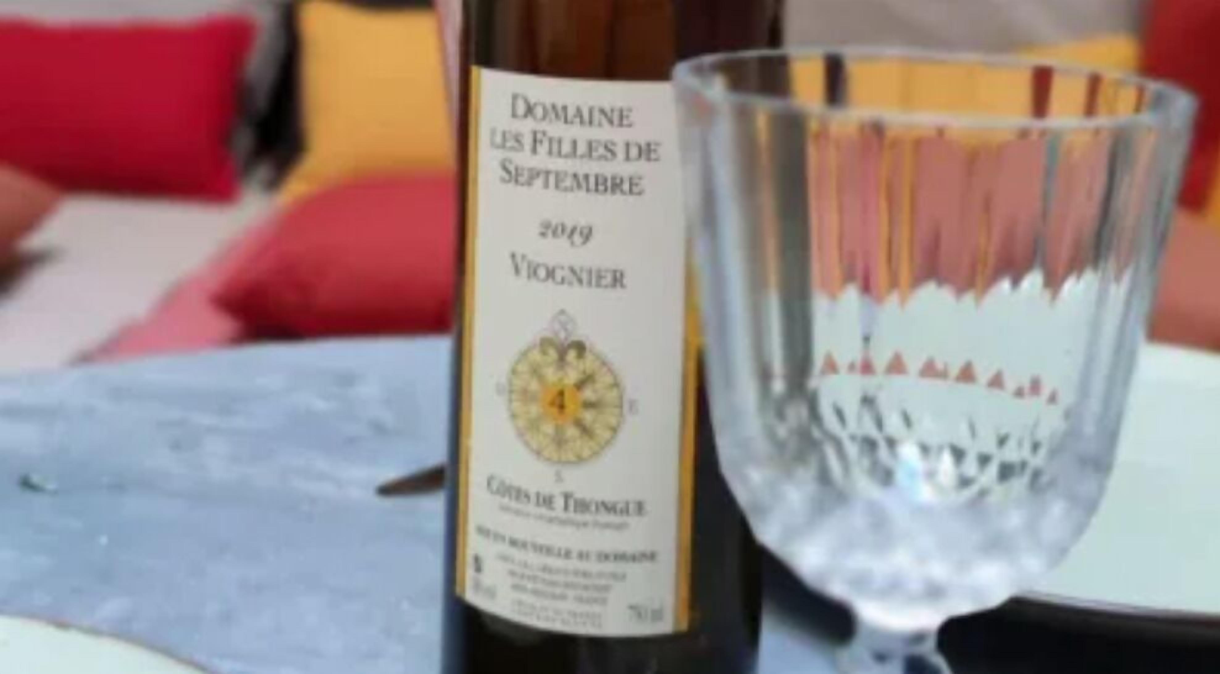 En flaske Domaine Les Filles de Septembre 2019 Vigneron vin ved siden af et tomt glas på et bord.