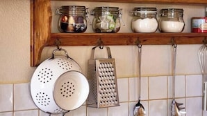 A kitchen with a tiled backsplash, a kettle, a colander, a grater, and hanging utensils. - The Studio (Valliguières)