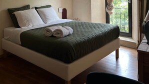 A bedroom with a bed, a bedside table, a lamp, and a window with curtains. - The Studio (Valliguières)